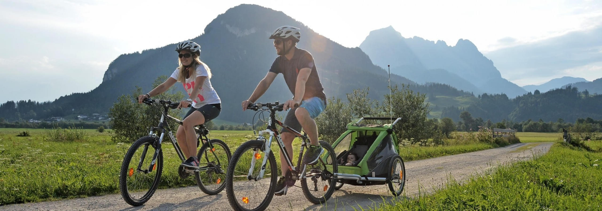 Familie beim Radfahren mit Kinderanhänger und Kleinkind in der Natur der Kitzbüheler Alpen