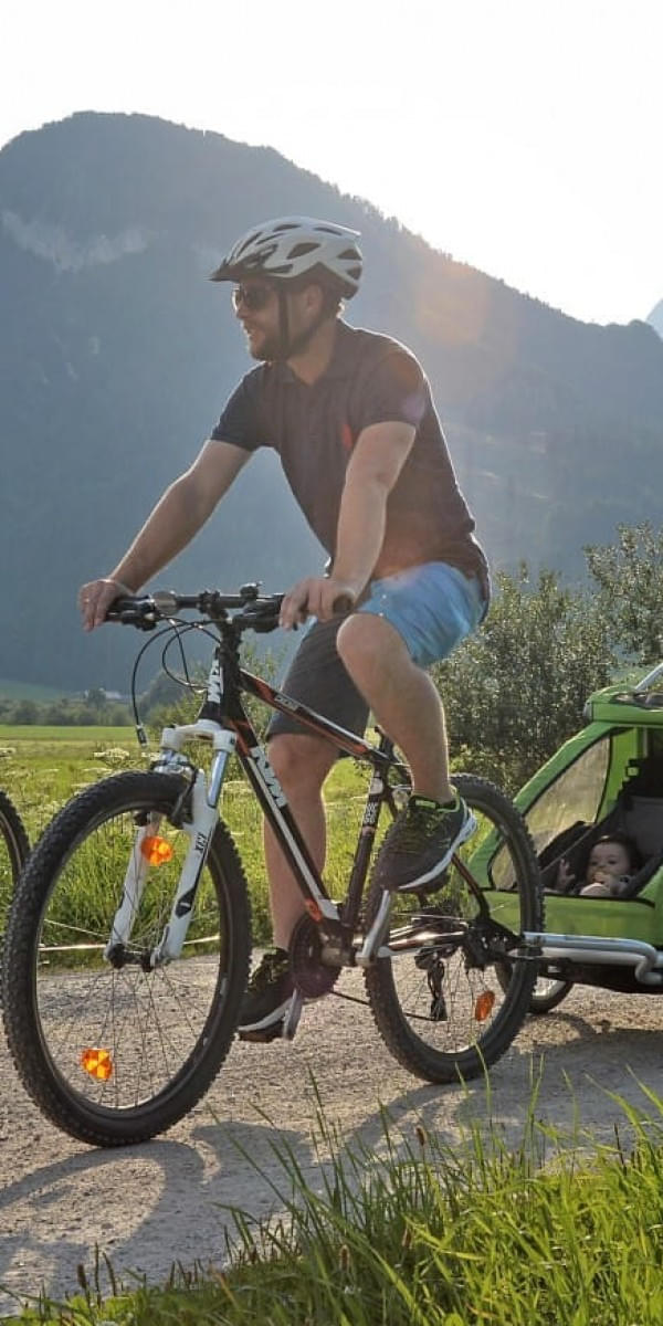 Familie beim Radfahren mit Kinderanhänger in der Landschaft der Kitzbüheler Alpen in Tirol