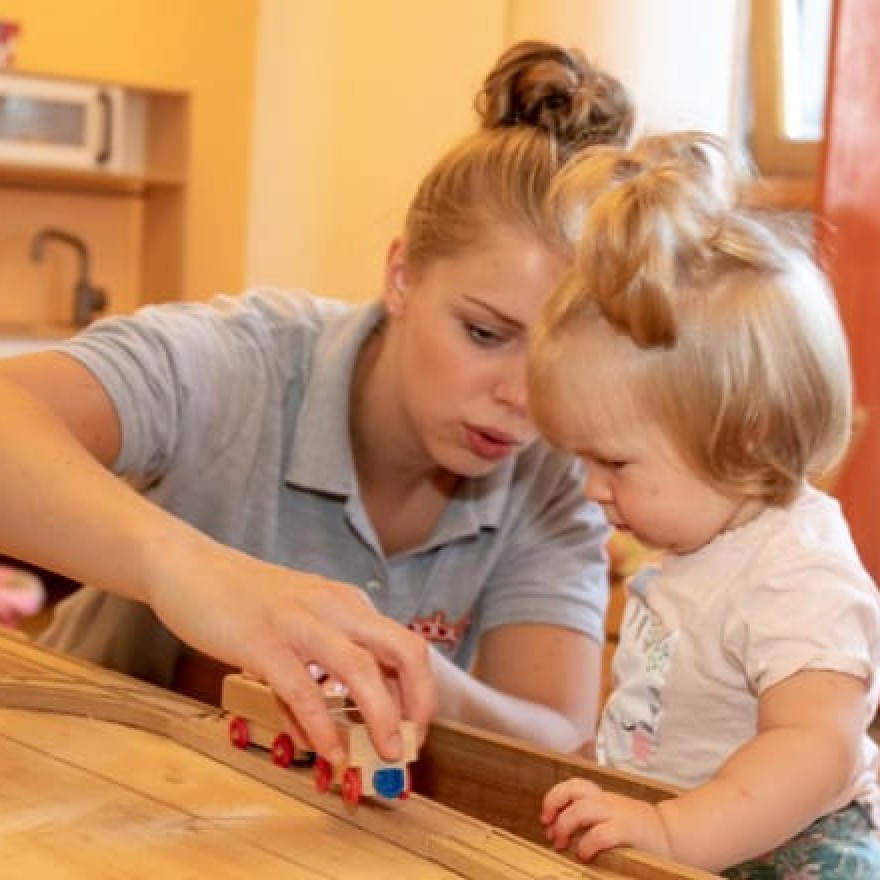 Betreuerin spielt mit Kleinkind im Baby- & Kinderhotel Babymio mit einer Holzlokomotive