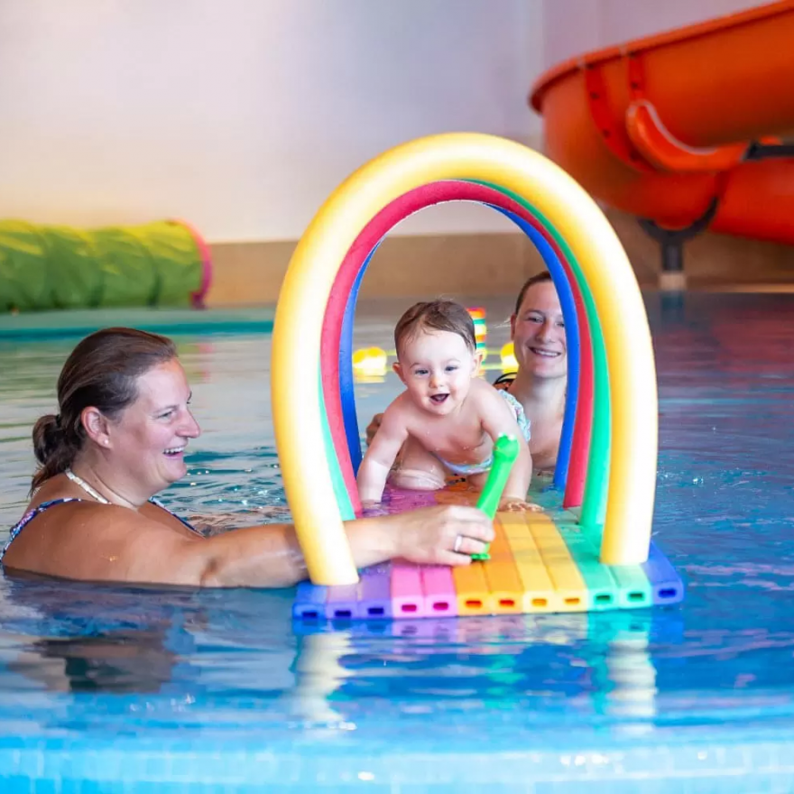 Eltern und Baby spielen im Pool mit buntem Wasserbogen