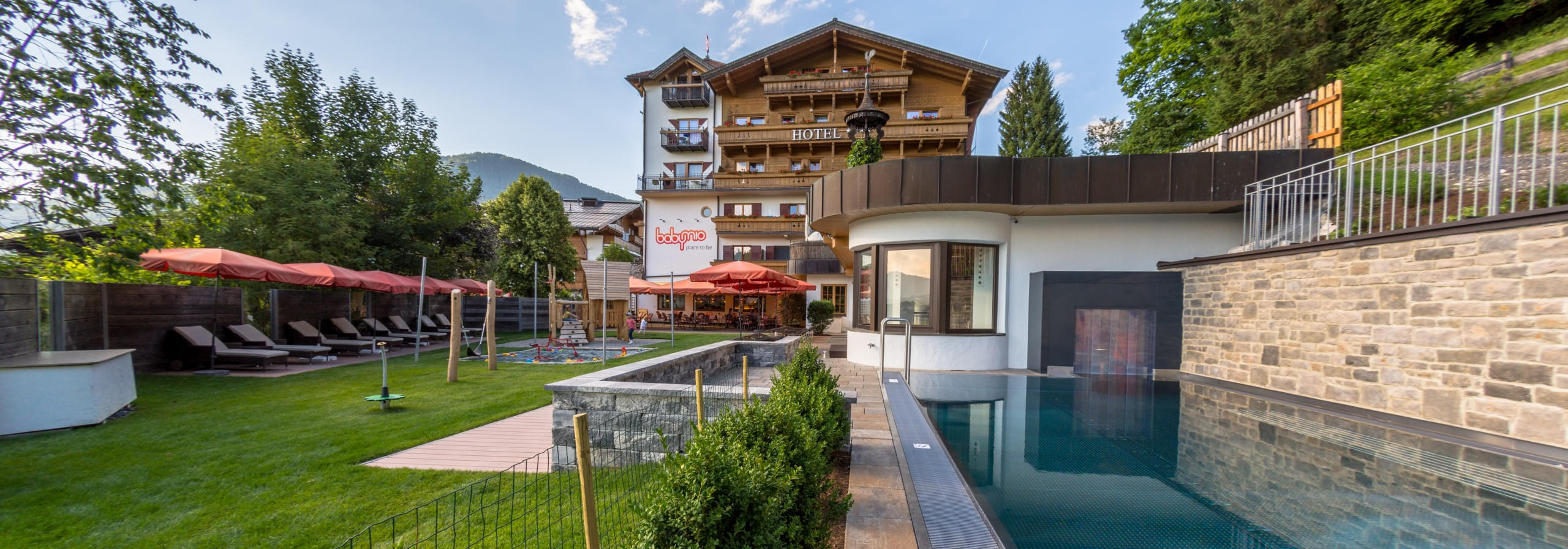 Außenansicht des Babyhotel und Kinderhotel Babymio mit Außenpool, Gartenbereich und Spielplatz
