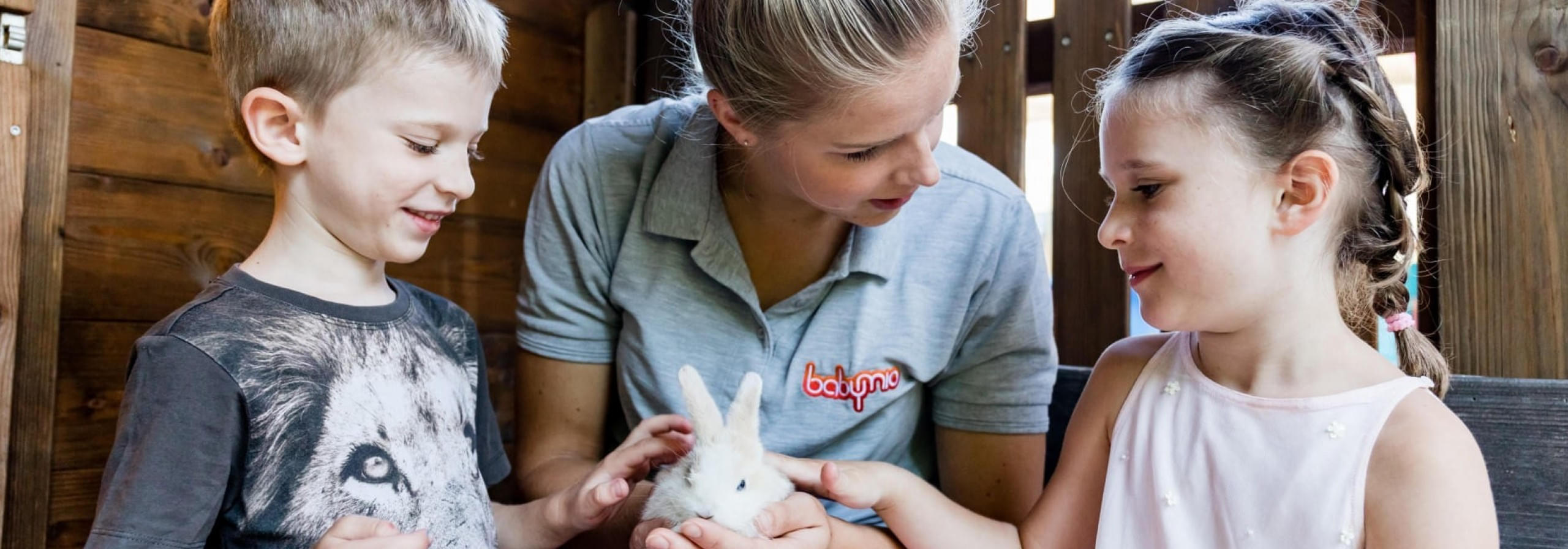 Betreuerin vom Hotel zeigt Kindern ein Kaninchen und sie streicheln es