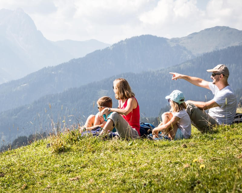 Familie sitzt auf einer Wiese und genießt den Blick auf die Berge der Kitzbüheler Alpen