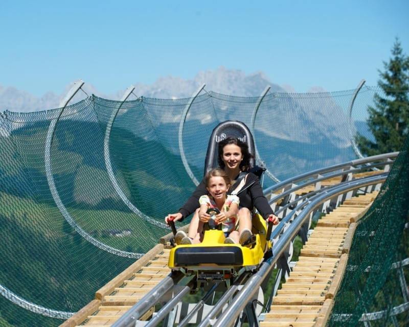 Mutter und Kind fahren mit der Sommerrodelbahn in den Bergen