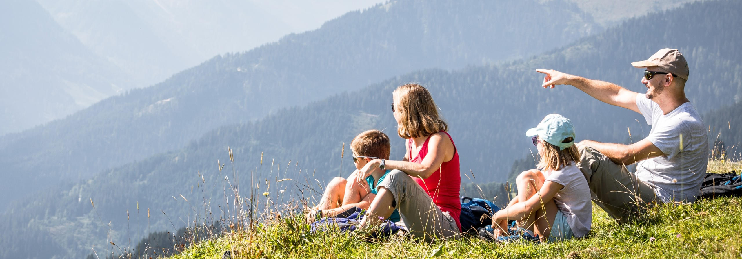 Familie sitzt auf einer Wiese und genießt den Blick auf die Berge der Kitzbüheler Alpen