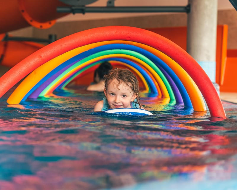 Kleinkind schwimmt im Pool durch bunte Schwimmreifen